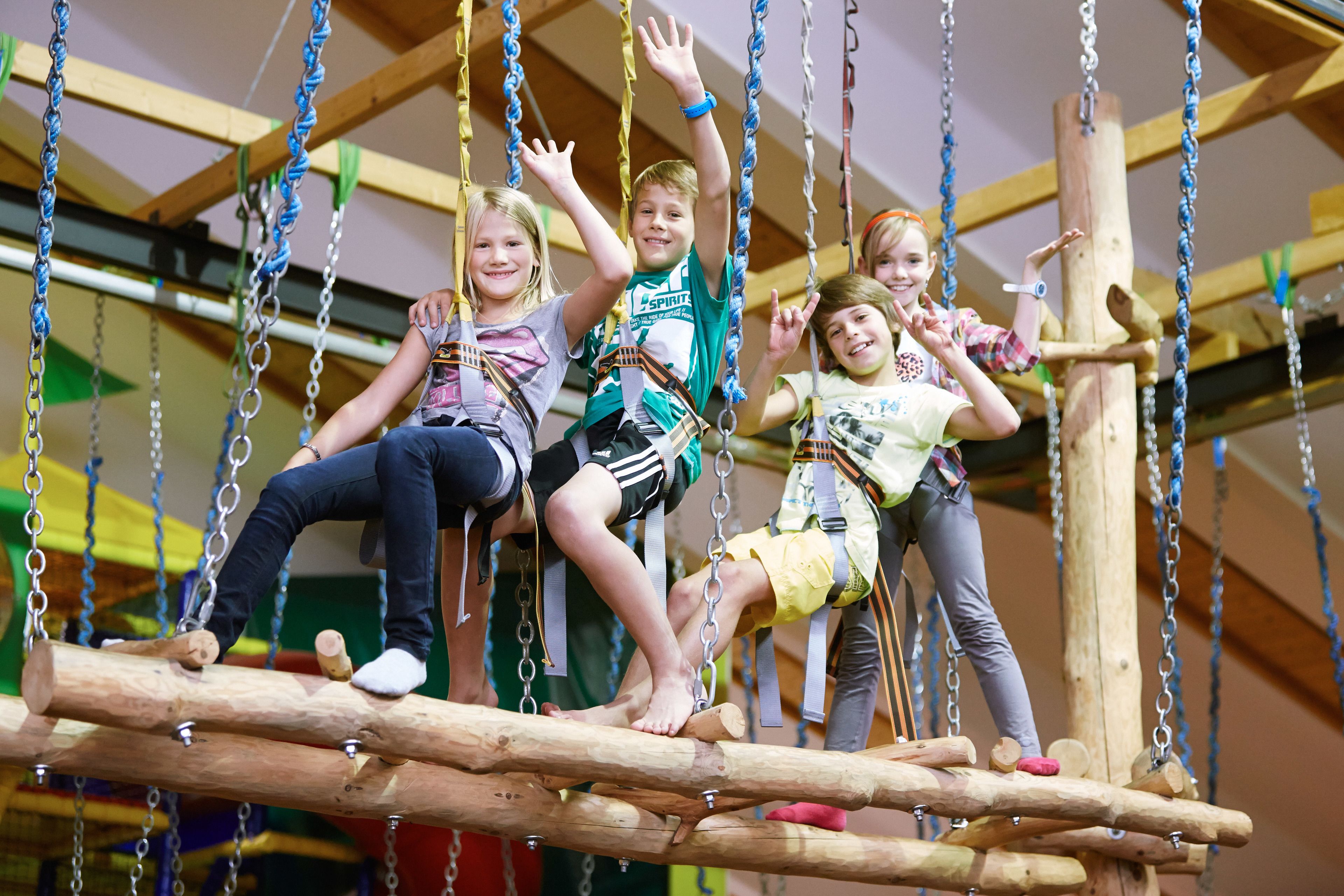 Children on a rope bridge with safety harnesses.