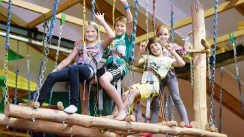 Children on a rope bridge with safety harnesses.