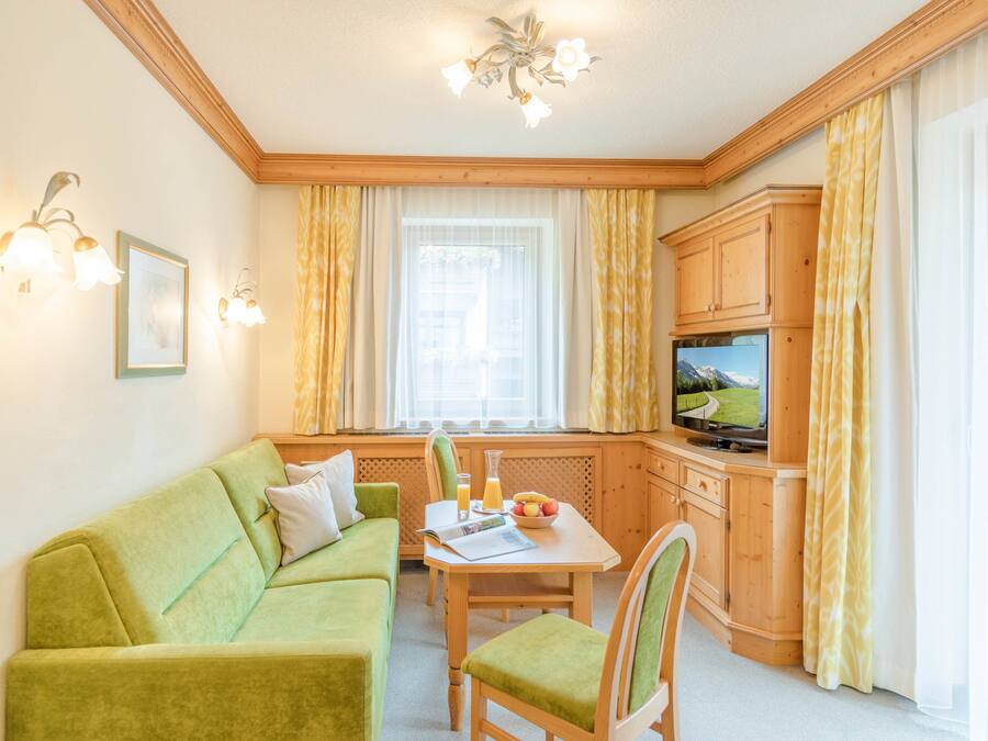 A cozy living room with a green sofa, wooden cabinet, and a television.