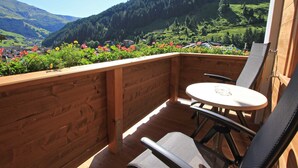 Un balcón de madera con una mesa y sillas, con vistas a un valle con montañas y un pueblo.