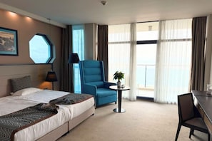 A hotel room with a bed, a blue armchair, a small table with a plant, and a desk. - Astera Hotel & Spa (Golden Sands)