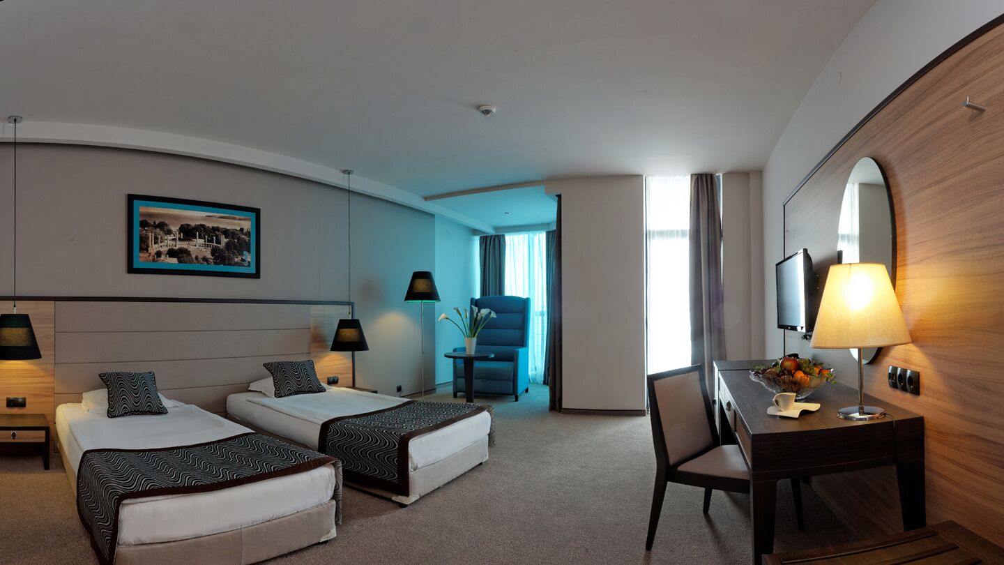 Une chambre d’hôtel avec deux lits, un bureau, une chaise, une télévision et un tableau au mur.
