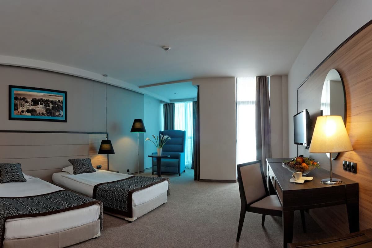 A hotel room with two beds, a desk, a chair, a TV, and a painting on the wall.