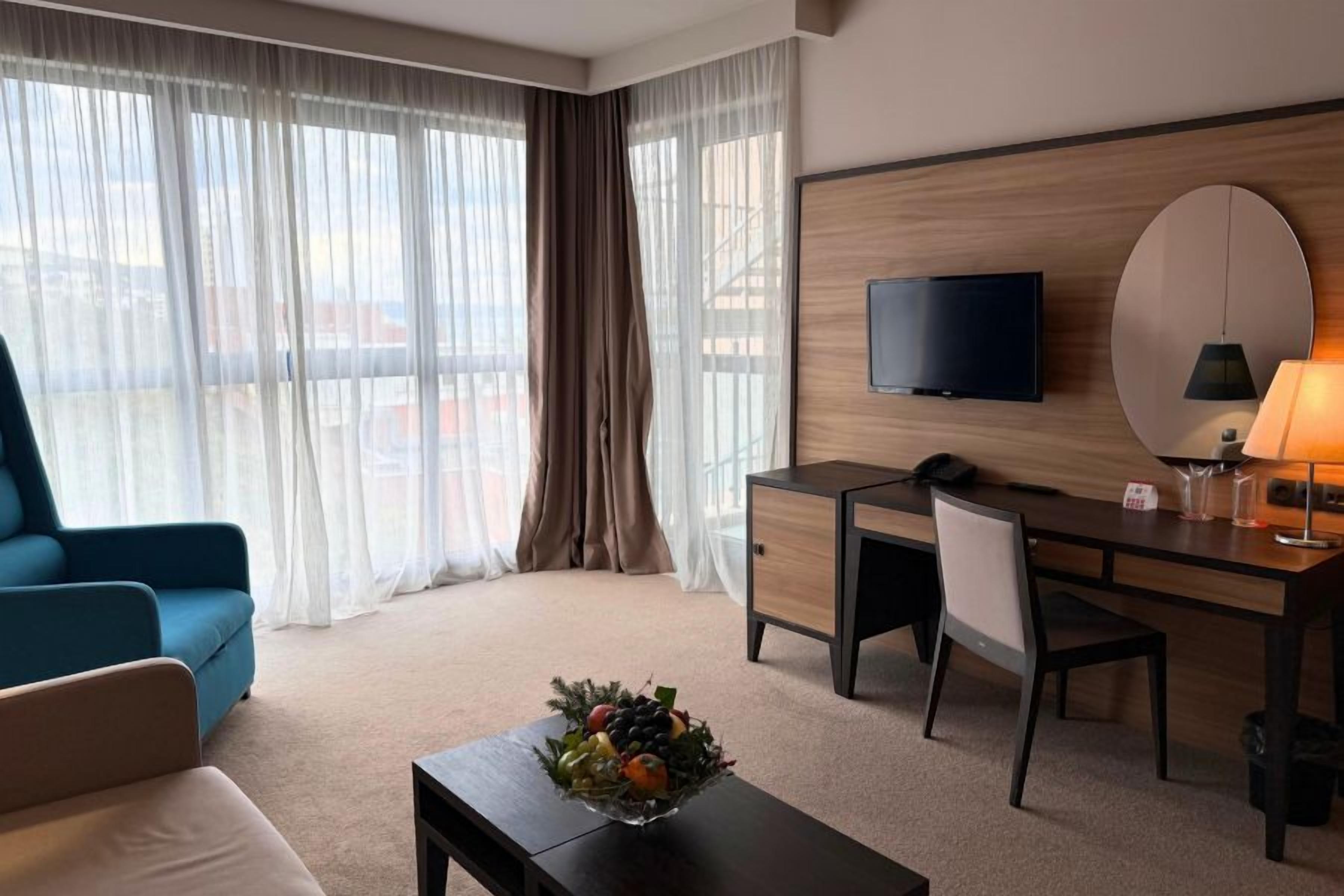 Een hotelkamer met een bed, een bureau, een stoel, een televisie, een lamp en een raam met gordijnen.