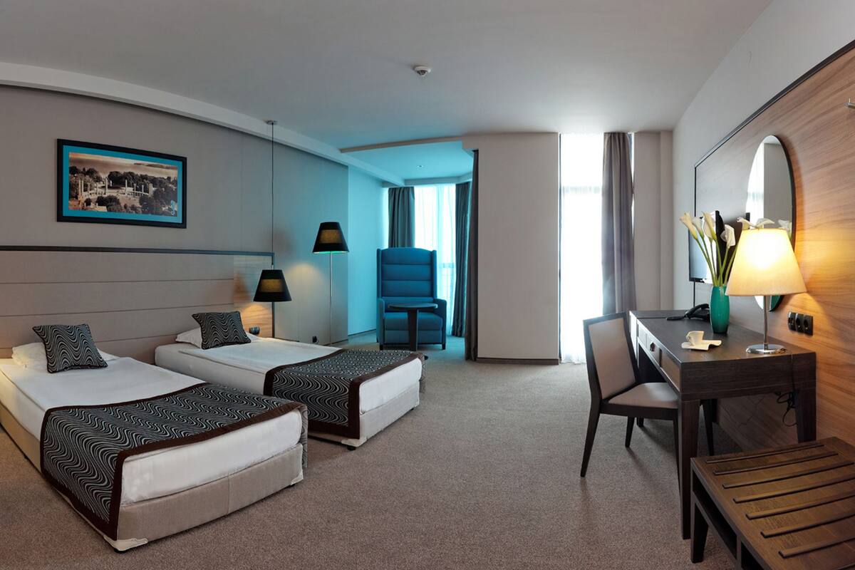 A hotel room with two beds, a desk, a chair, a lamp, and a large mirror.