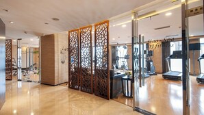A modern gym with exercise equipment, a reception area, and a glass partition with decorative panels. - Regal Jinfeng Hotel (Shanghai)