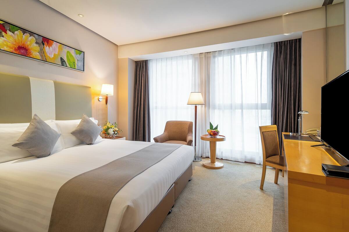 A hotel room with a large bed, a desk, a chair, a TV, and a painting on the wall.