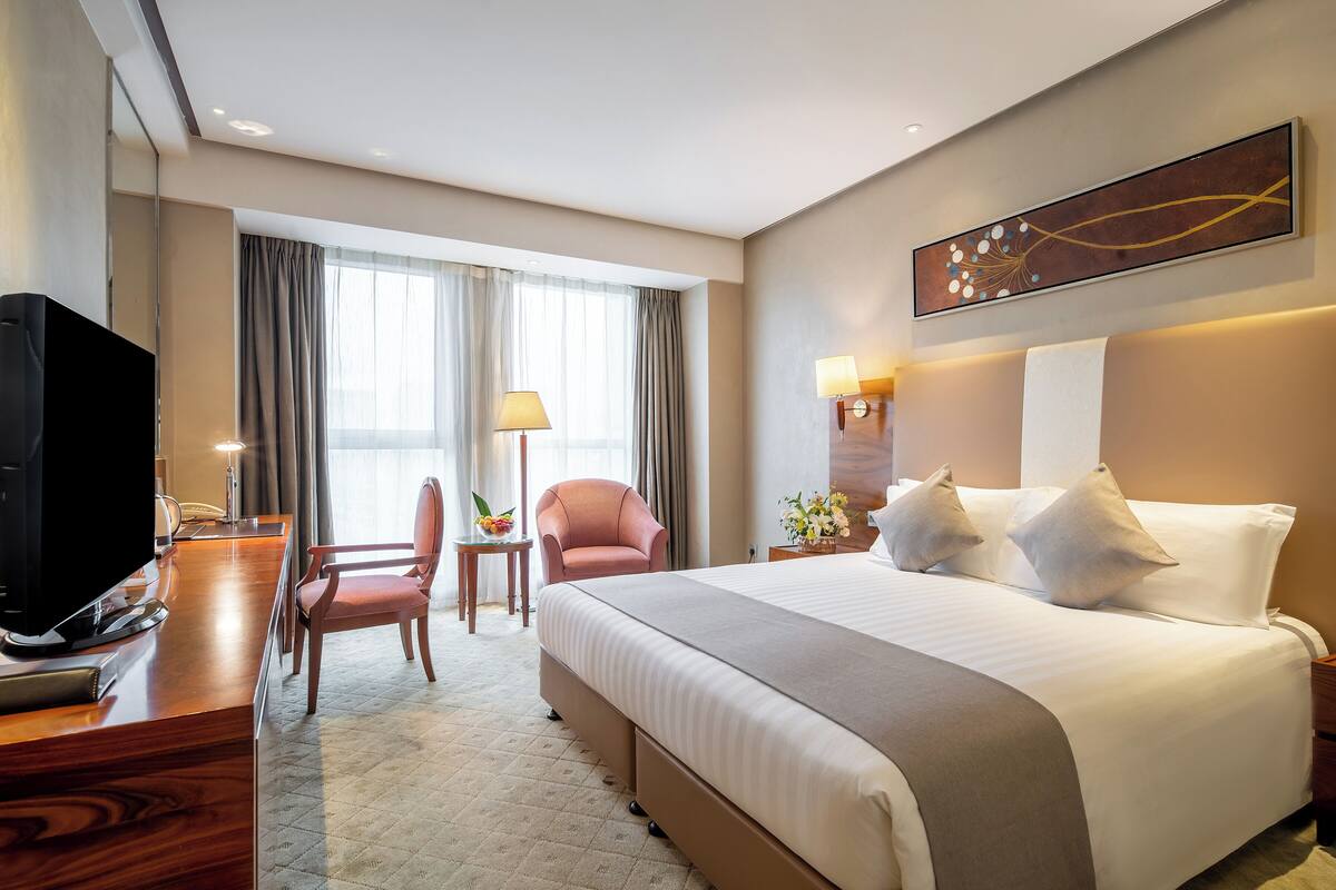 A hotel room with a large bed, a desk with a television, a chair, and a window with curtains.