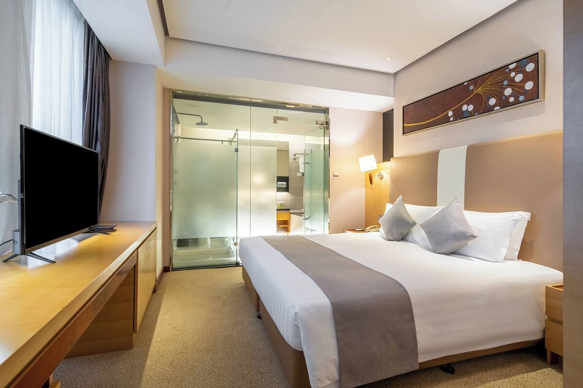 A hotel room with a bed, bedside table, TV, and a walk-in closet.