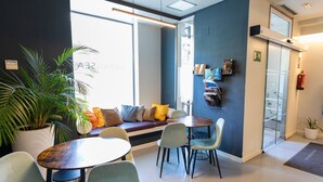 A modern office space with a large window, a seating area with a sofa and chairs, a small table, and a potted plant. - Urban Sea Atocha 113 (Madrid)