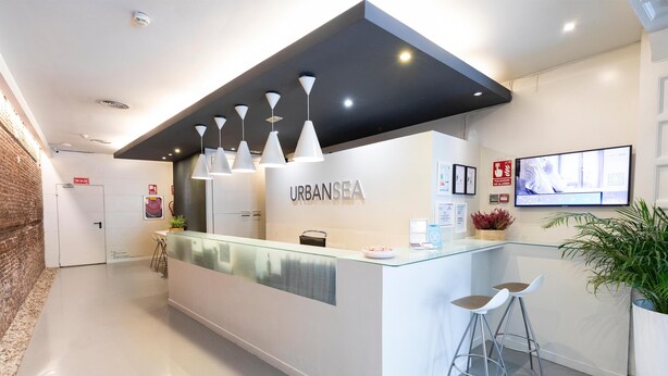 A reception area with a glass counter, white bar stools, and a mounted TV. - Urban Sea Atocha 113 (Madrid)