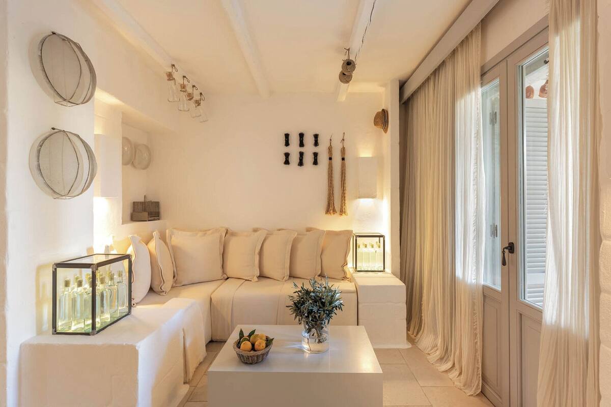 A modern living room with a beige sofa, a coffee table with fruits and a vase, and decorative items on the walls.