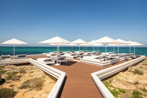 A beachside lounge area with white umbrellas and lounge chairs, a wooden deck, and a clear view of the sea. - Borgo Egnazia (Fasano)