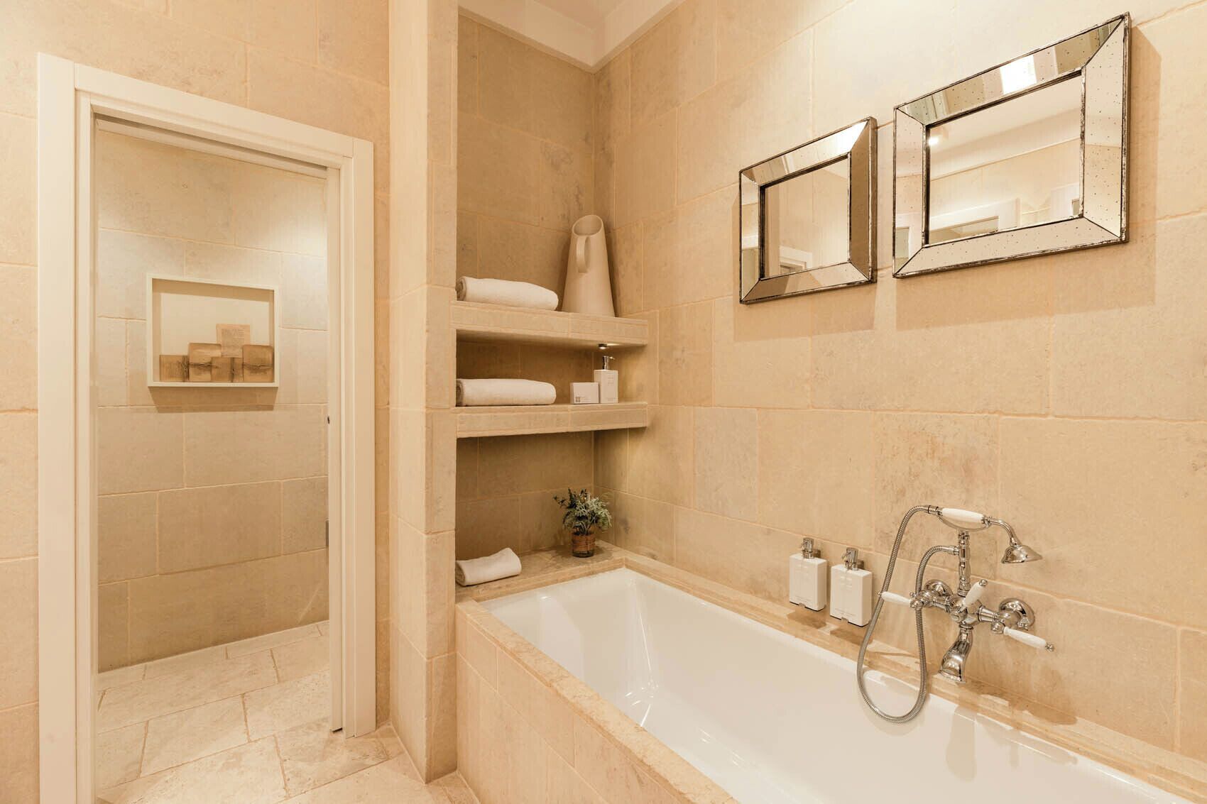 A bathroom with a bathtub, shelves with towels, and two mirrors on the wall.