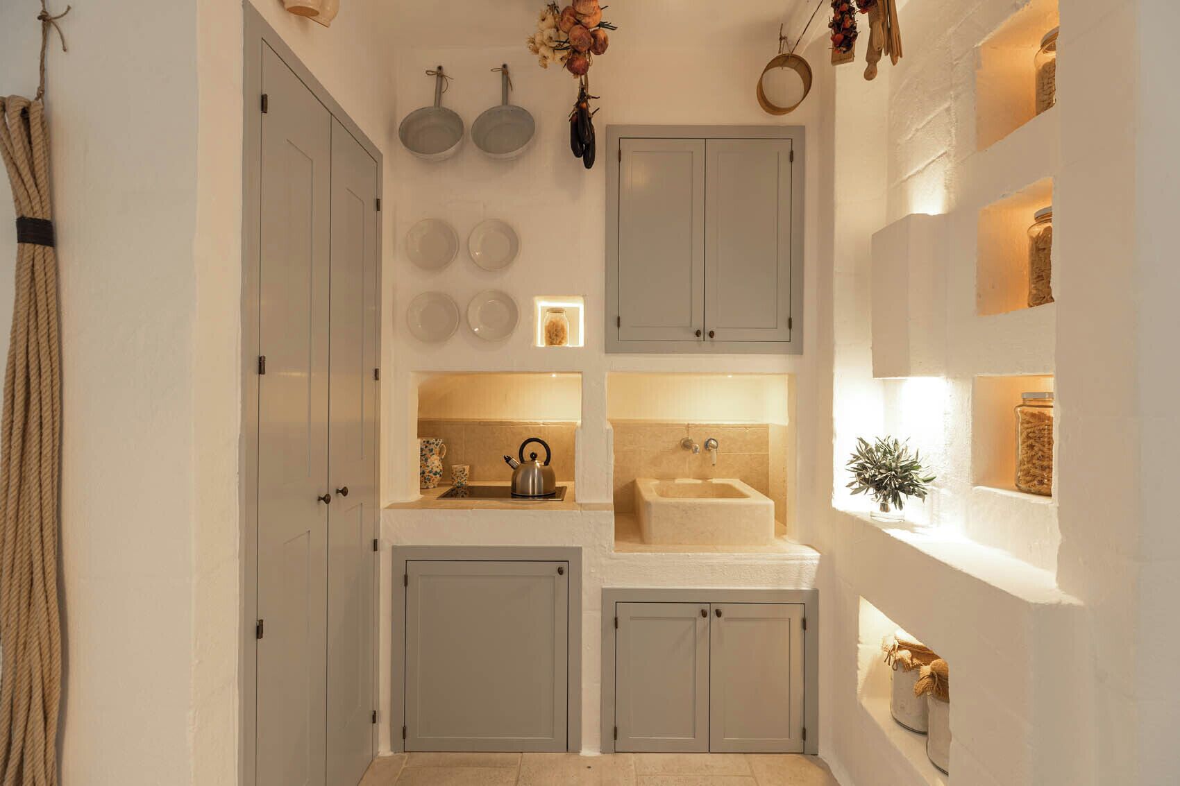 Una cucina compatta con lavandino, bollitore e oggetti decorativi sugli scaffali.