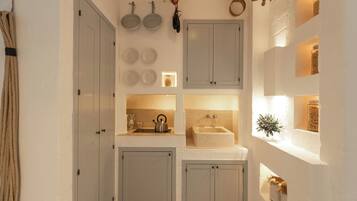 Una cucina compatta con lavandino, bollitore e oggetti decorativi sugli scaffali.