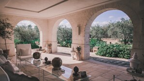 A sunlit patio with a glass table, a sofa, and a view of a garden through arches. - Borgo Egnazia (Fasano)