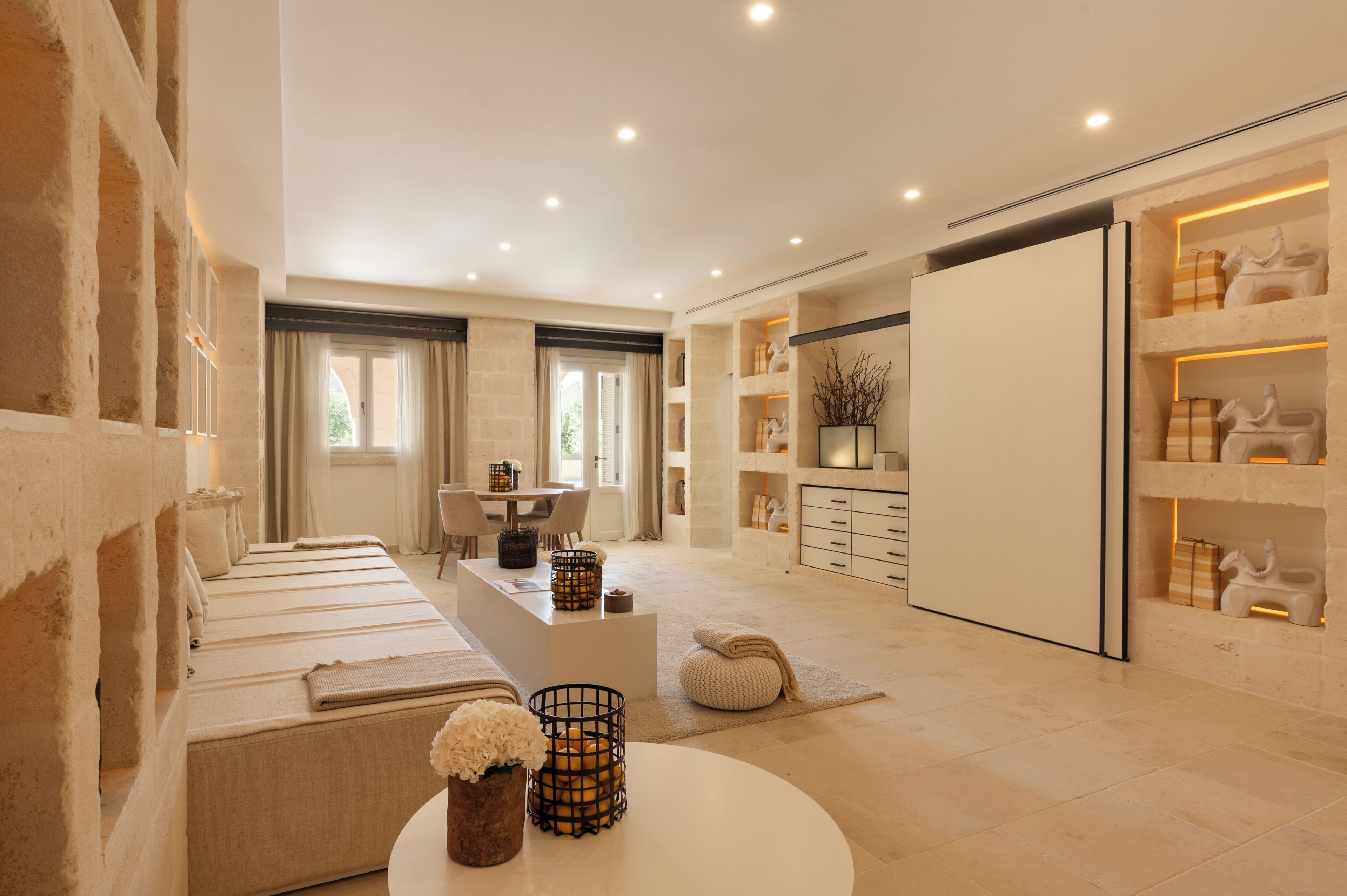 A modern hotel room with a large bed, a sitting area, a dining table, and a wardrobe.