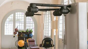 Een sportschool met trainingsapparatuur, grote ramen en een deur.