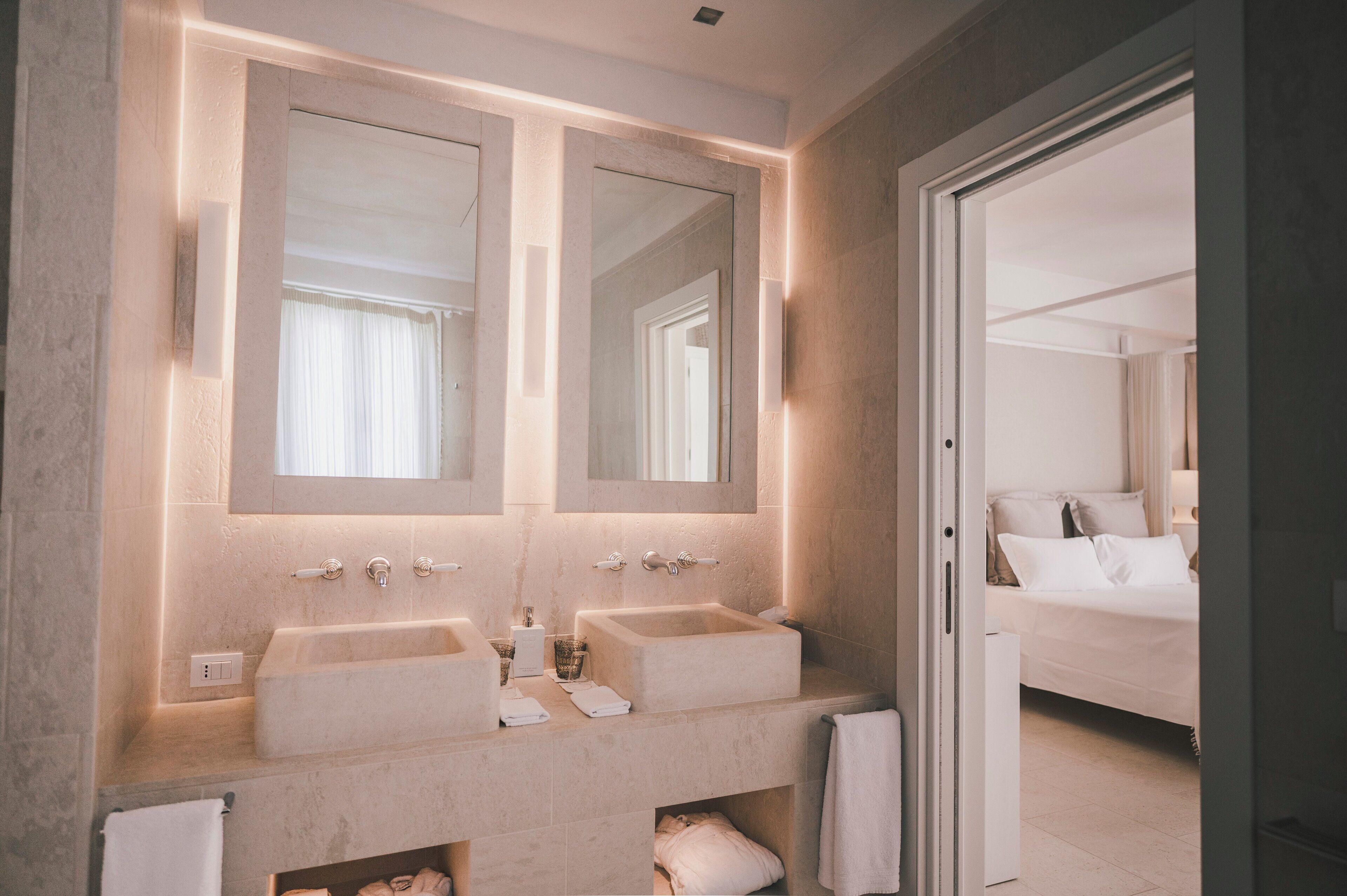 A modern bathroom with two sinks, a large mirror, and a walk-in closet.
