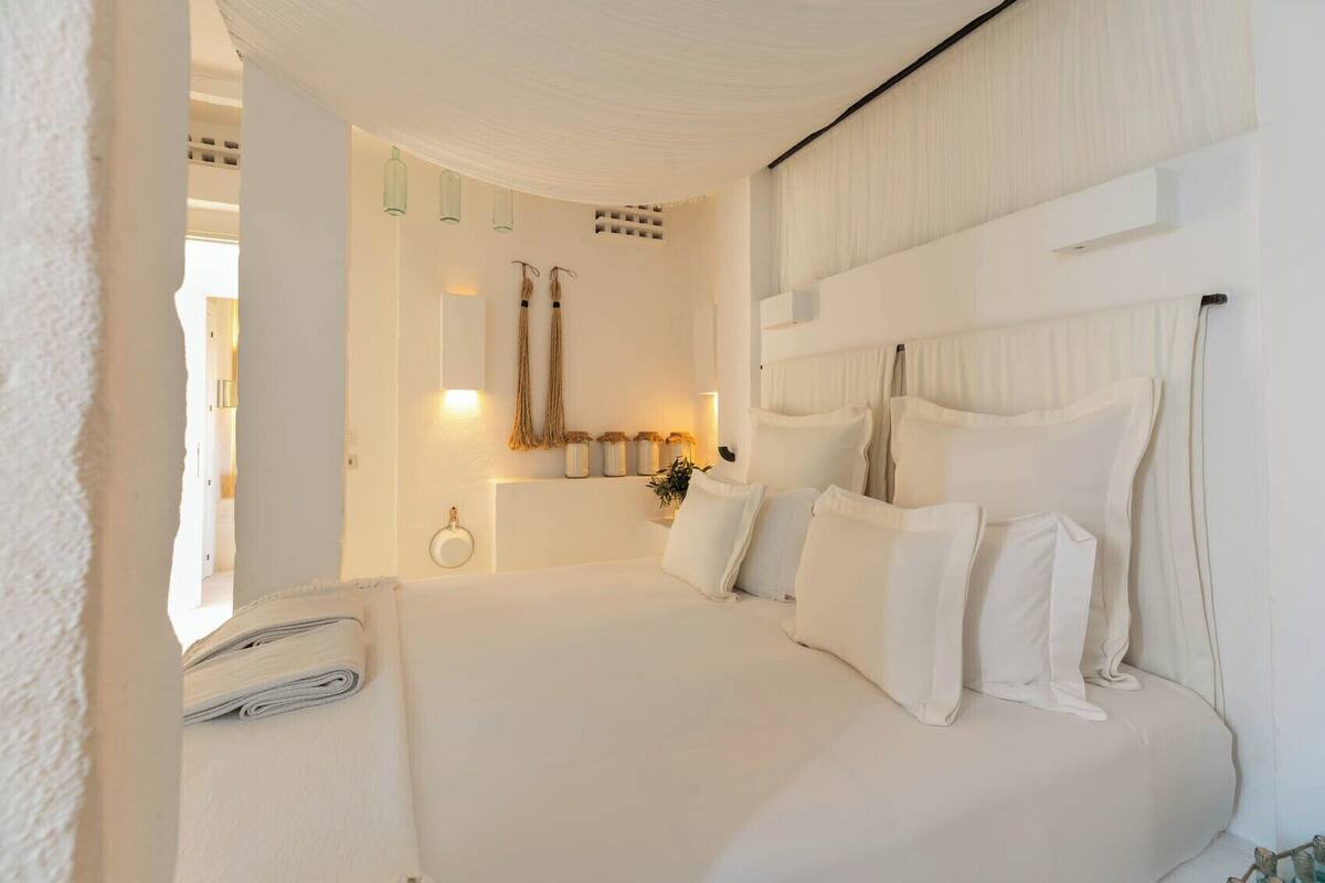A bedroom with a large bed, a bedside table, and a wall-mounted shelf with jars.