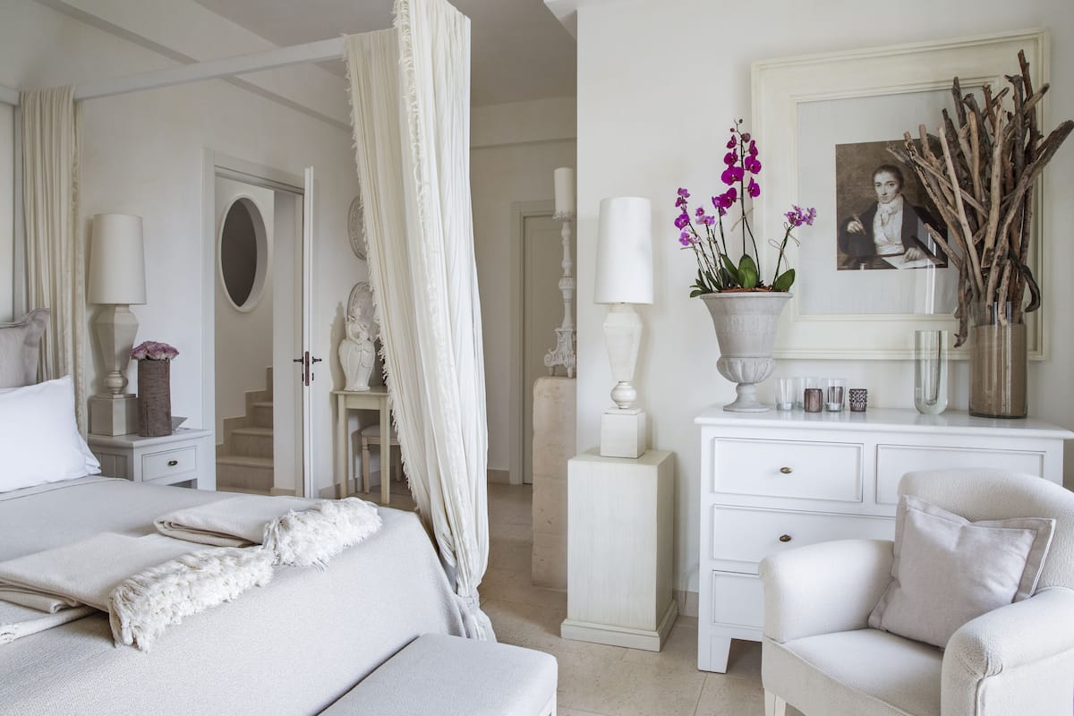 A bedroom with a bed, a chair, a nightstand, a dresser, a mirror, and a door.