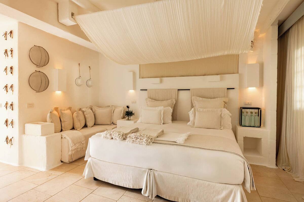A spacious bedroom with a large bed, a sofa, and a wall-mounted light fixture.