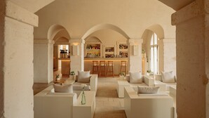 A spacious lounge area with white sofas, a bar with stools, and a view of the bar area through arched ceilings. - Borgo Egnazia (Fasano)