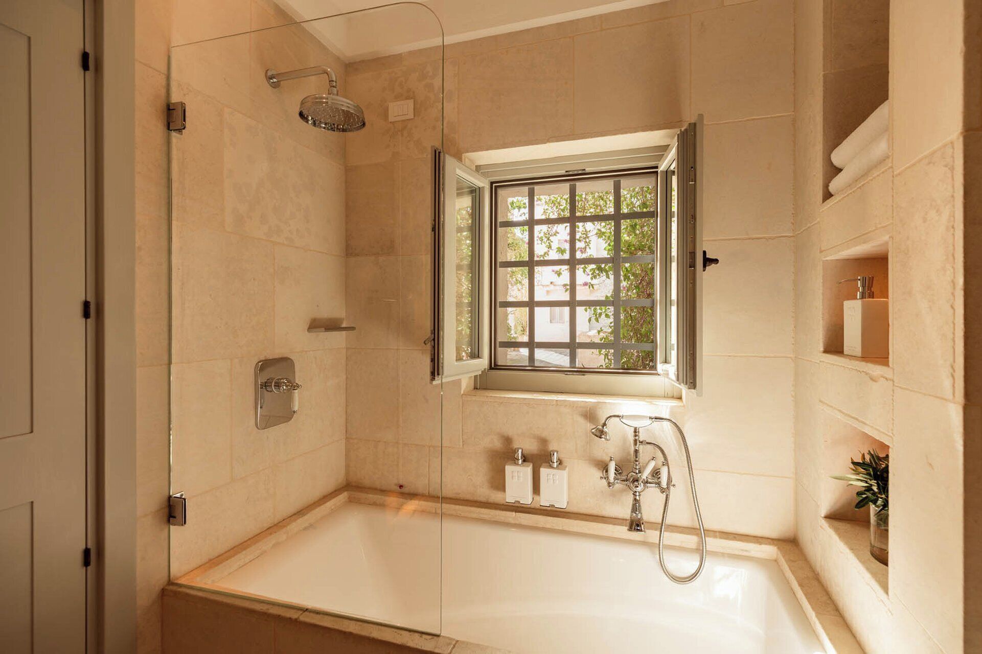 A modern bathroom with a bathtub, a shower, and a window with a view of greenery outside.