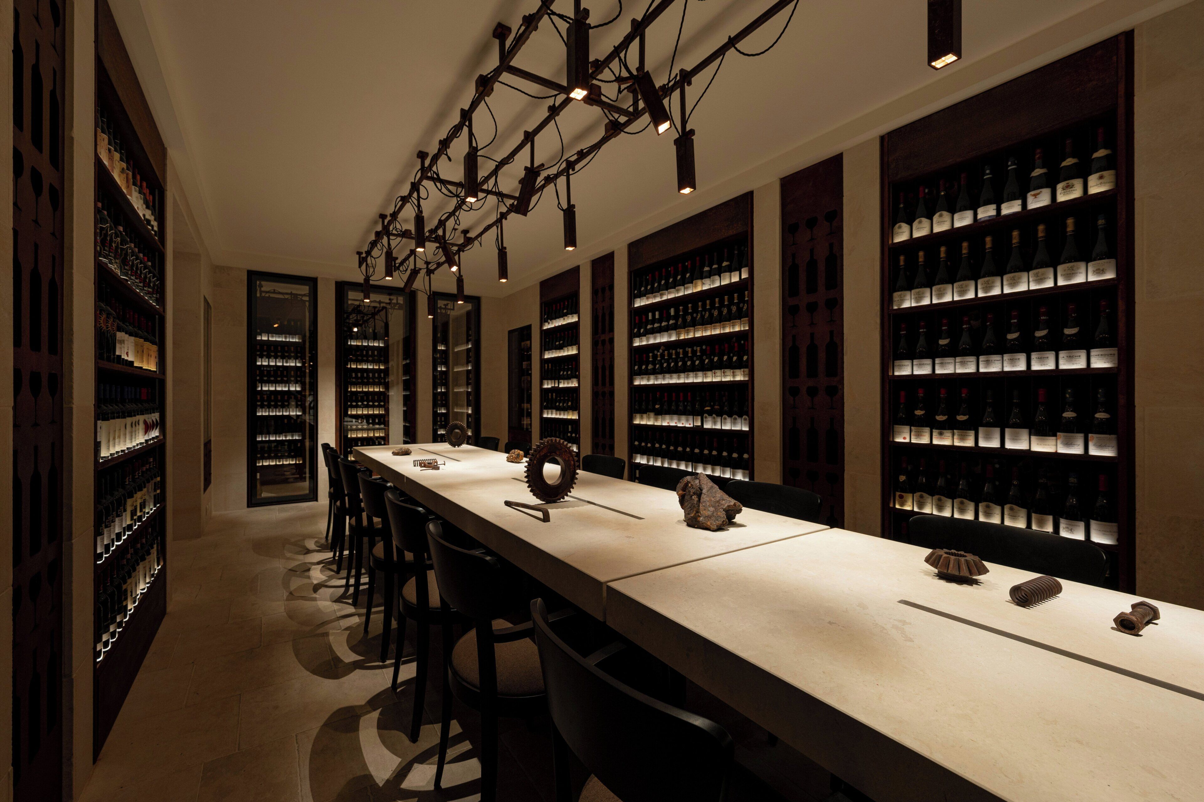 Una sala alargada y estrecha con una mesa central y sillas, rodeada de estantes llenos de botellas de vino.