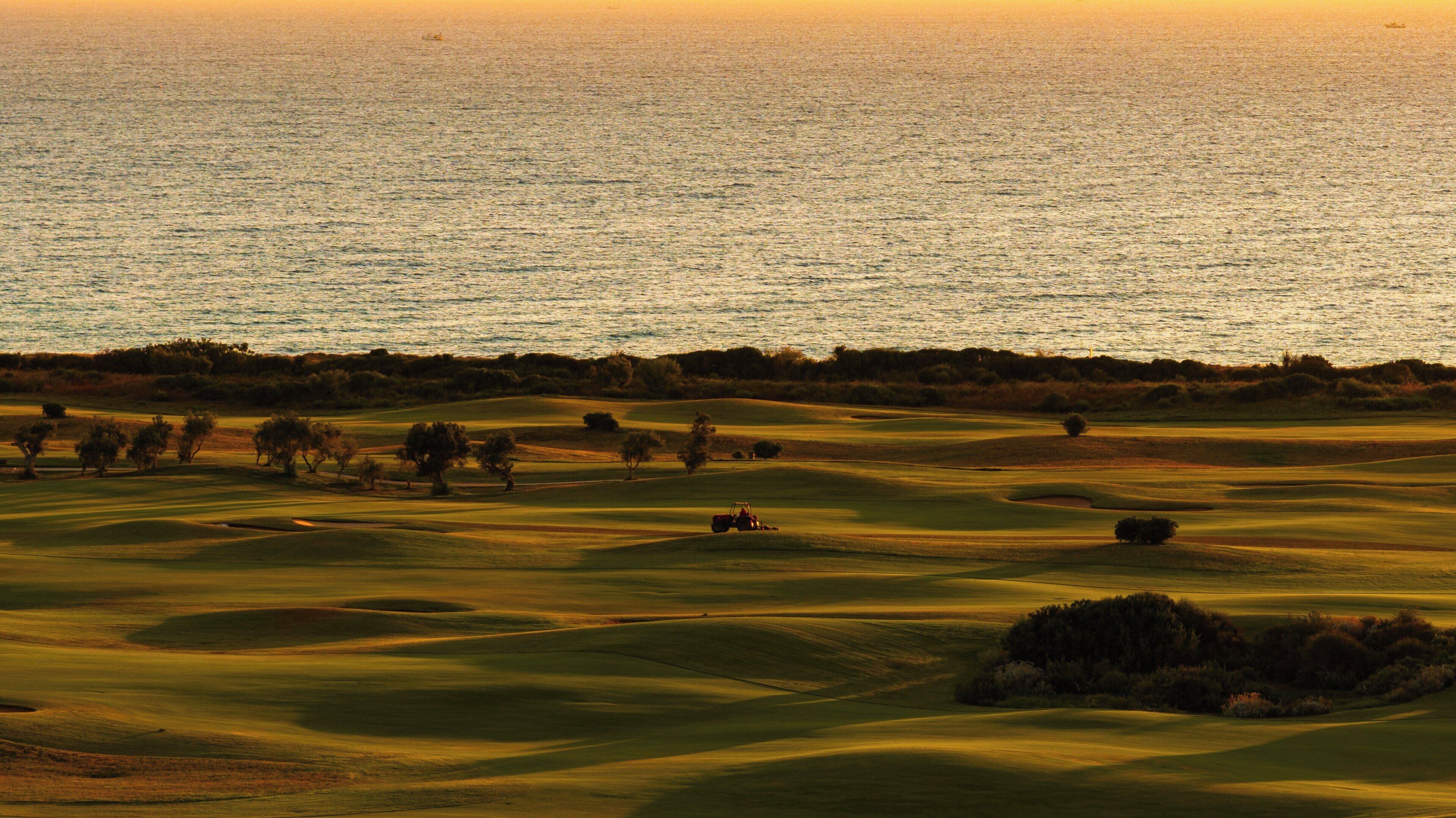 A golf course with a view of the ocean at sunset.
