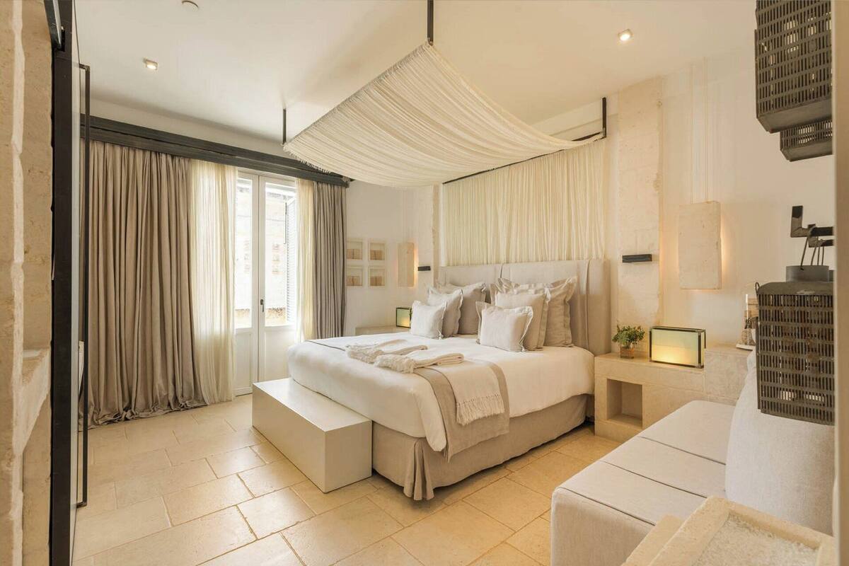 A spacious bedroom with a large bed, a bench, and a bedside table with a lamp.