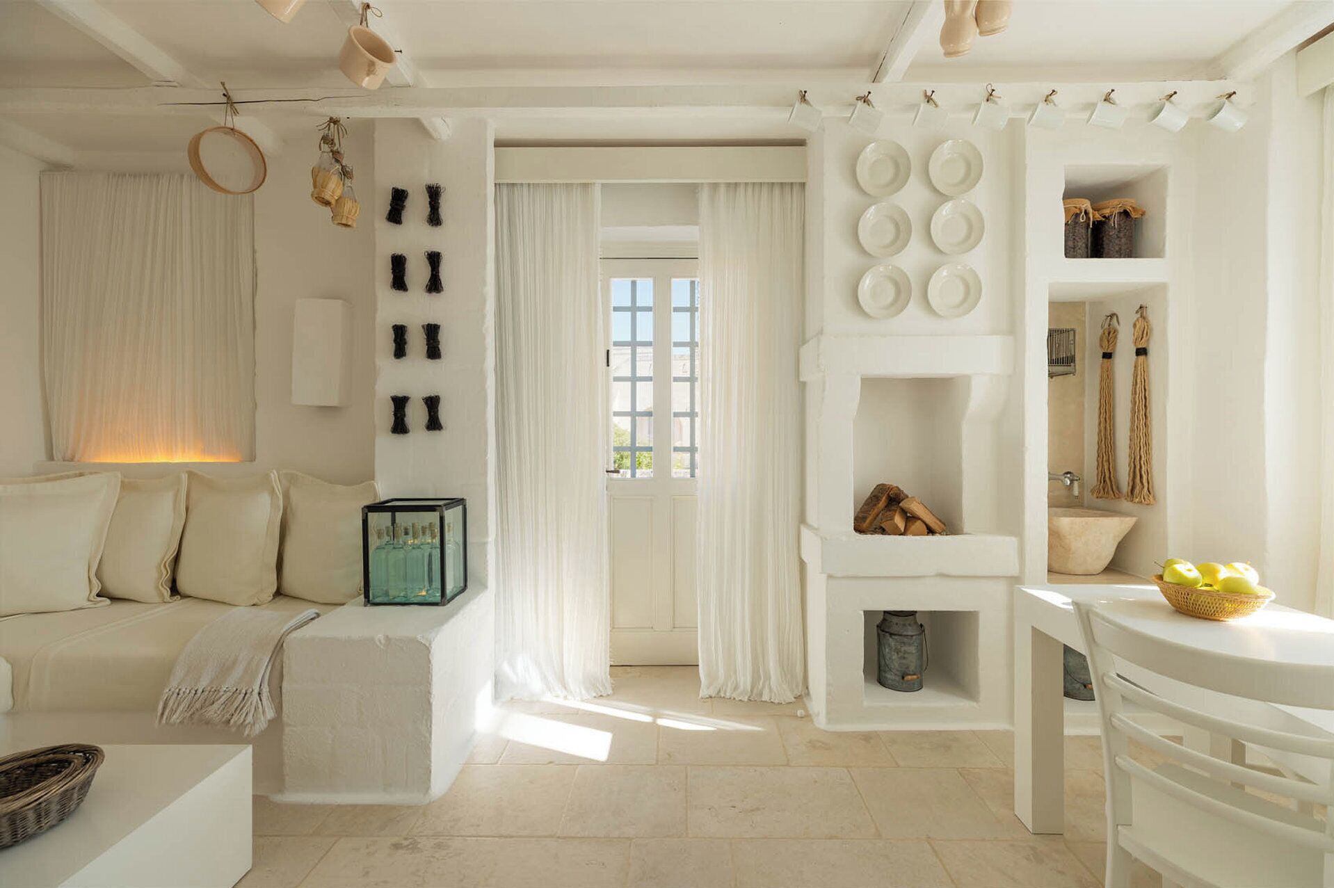 A minimalist white room with a sofa, a table, and a window with curtains.