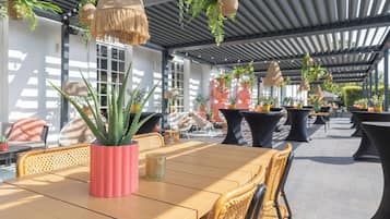 Een terras buiten met houten tafels en stoelen, plantenpotten en hangmanden.