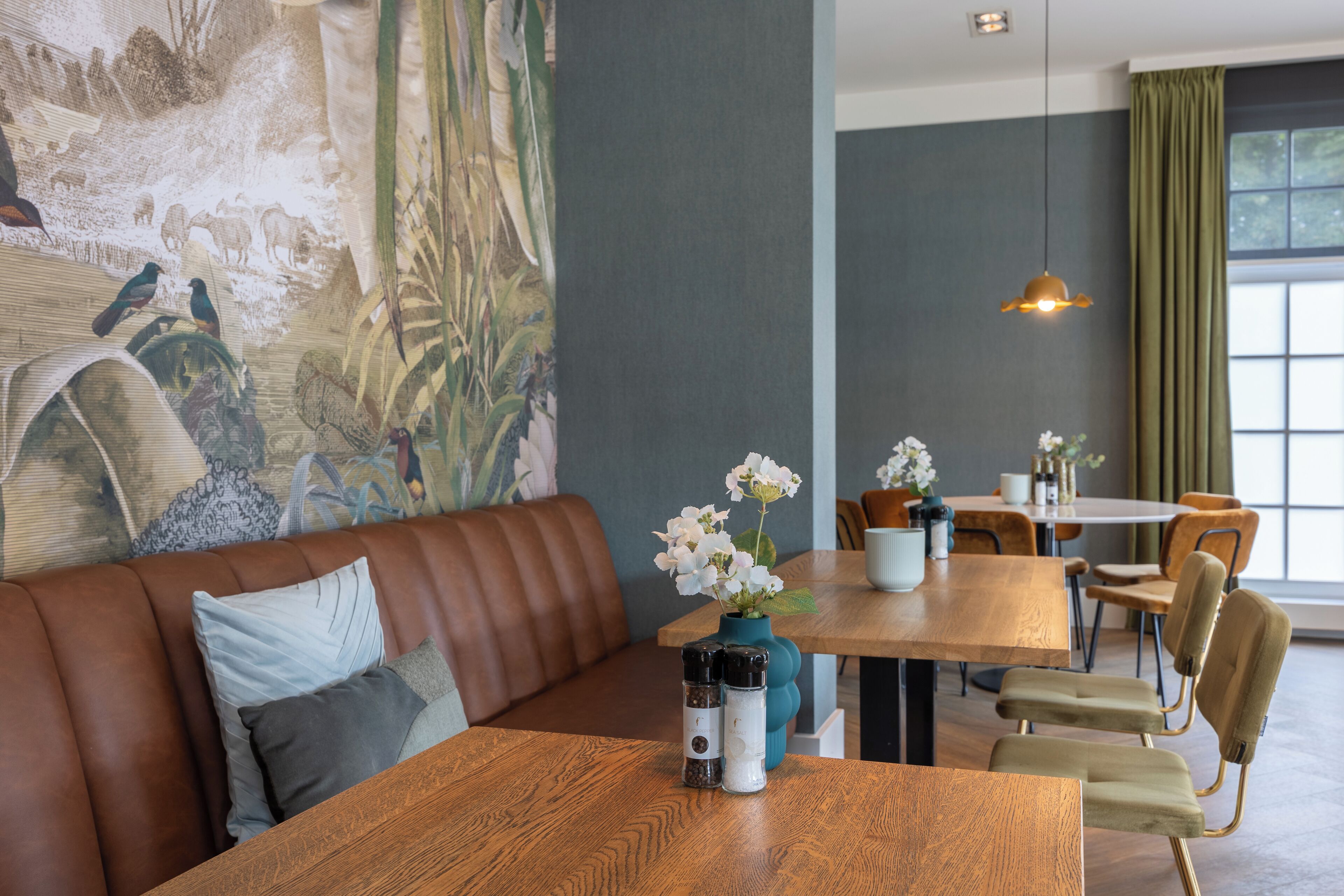 A restaurant with a wooden table, a brown leather couch, and a mural on the wall.