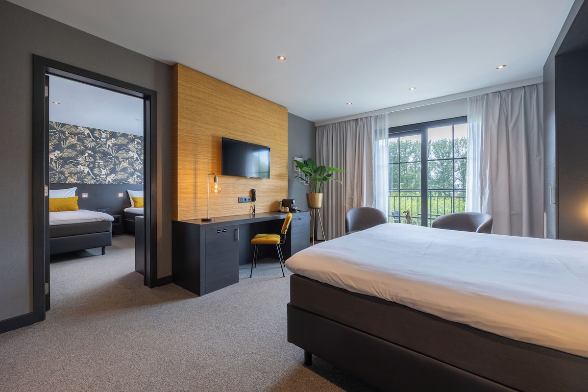 A modern hotel room with a large bed, a desk, a chair, a TV, and a window with curtains.