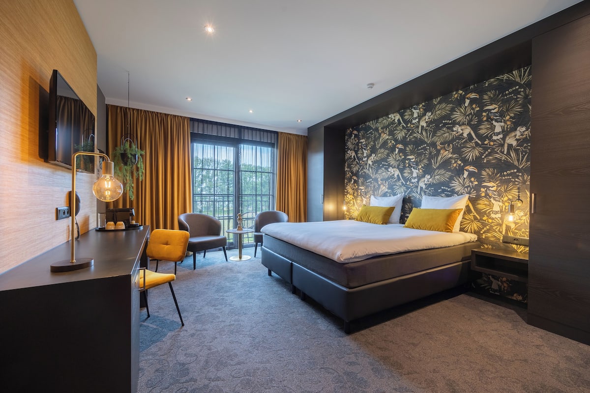 A modern hotel room with a large bed, a desk, two chairs, and a TV.