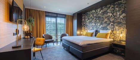 A modern hotel room with a large bed, a desk, two chairs, and a TV.