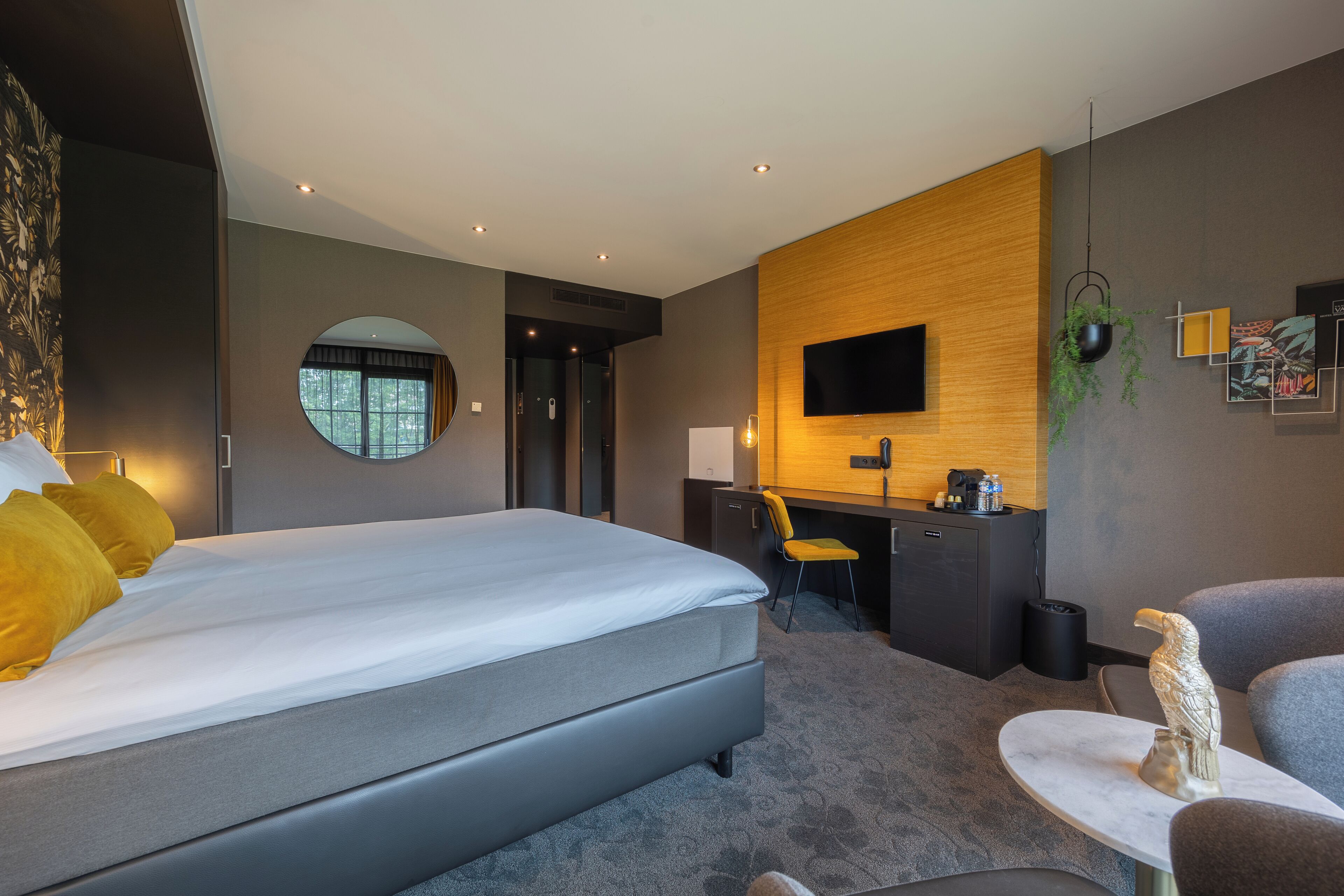 A modern hotel room with a large bed, a desk, a chair, a TV, and a small table with a decorative item.