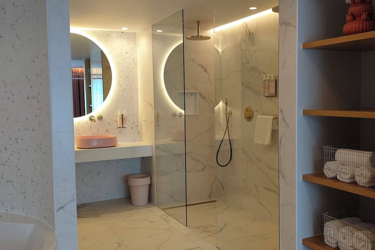 A modern bathroom with a glass-enclosed shower, a round mirror, and marble flooring.