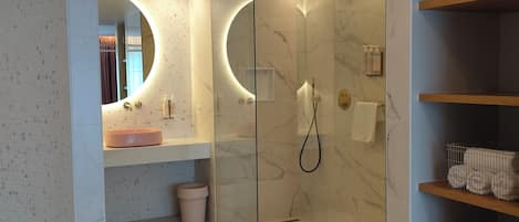 Un baño moderno con ducha de vidrio, un espejo redondo y suelo de mármol.