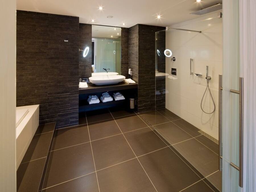 Une salle de bain moderne avec un grand miroir, un lavabo rond, une douche en verre et un carrelage foncé.