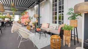 Un espacio al aire libre con mobiliario de mimbre, plantas en macetas y una alfombra estampada.
