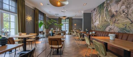 Un restaurante espacioso con techos altos, iluminación colgante y un gran mural con fauna tropical.