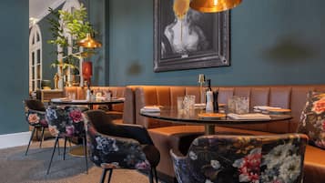 Un área de comedor con asientos tipo cabina, una mesa con un florero y un salero, y una obra de arte grande enmarcada en la pared.