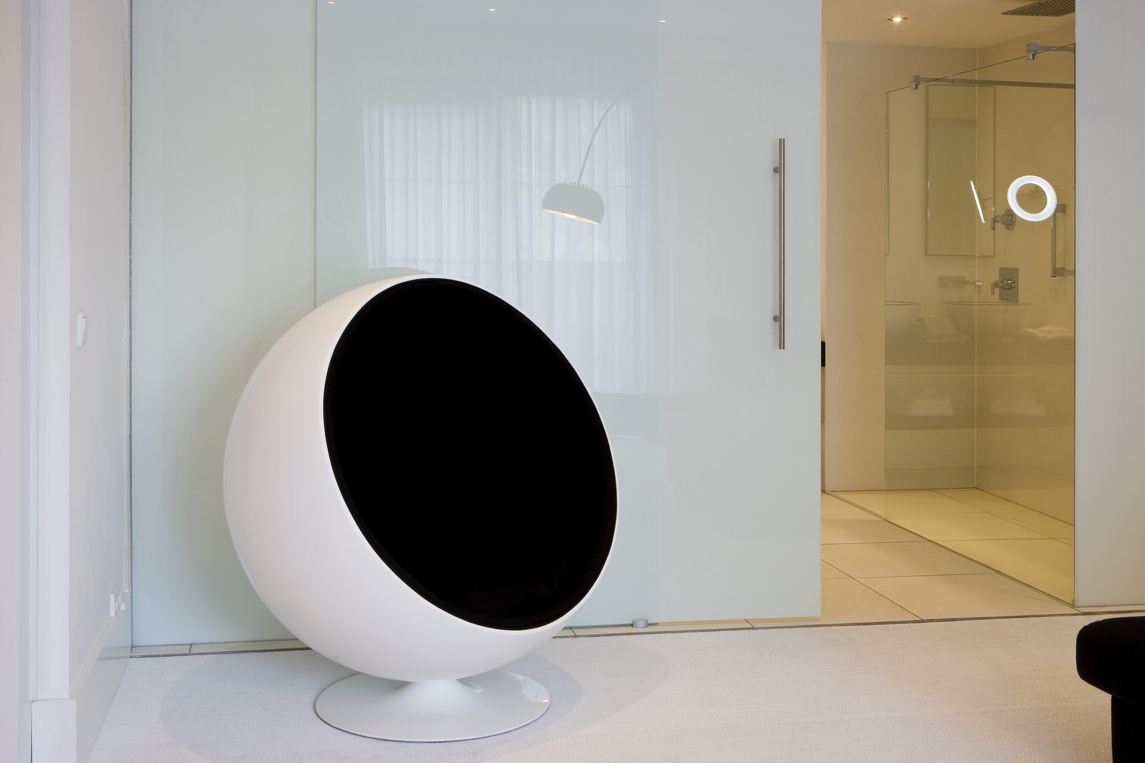Un interno moderno con una poltrona sferica, un divisorio in vetro e un bagno minimalista.