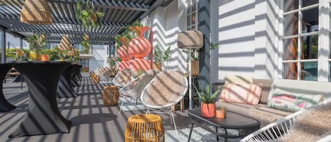 An outdoor seating area with modern furniture, including a sofa, chairs, and a table, surrounded by potted plants and decorative elements.
