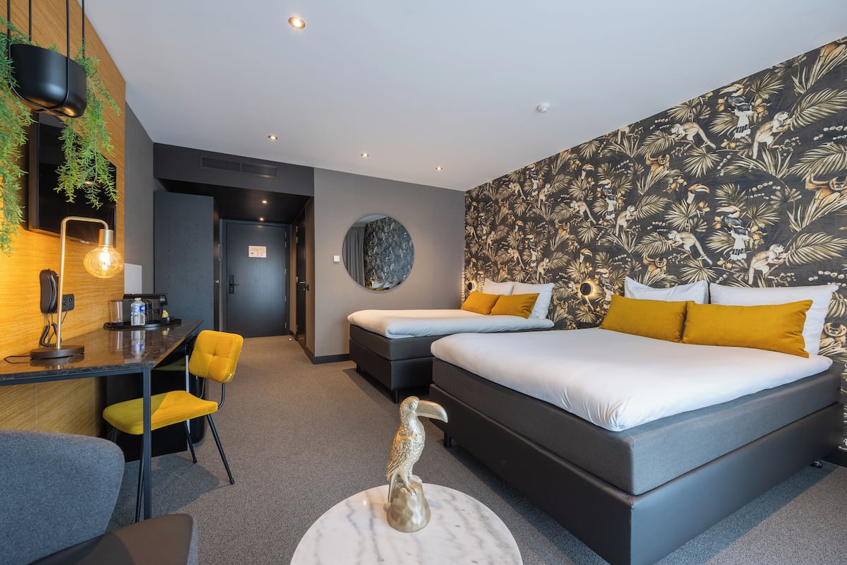 A modern hotel room with a large bed, a desk with a chair, and a small table with a decorative bird sculpture.