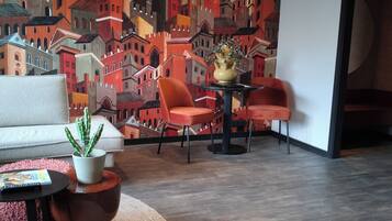 Ein modernes Wohnzimmer mit Stadtkulissen-Wandgemälde, einem weißen Sofa, zwei orangefarbenen Sesseln, einem kleinen Tisch mit Pflanze und einem runden gewebten Teppich.