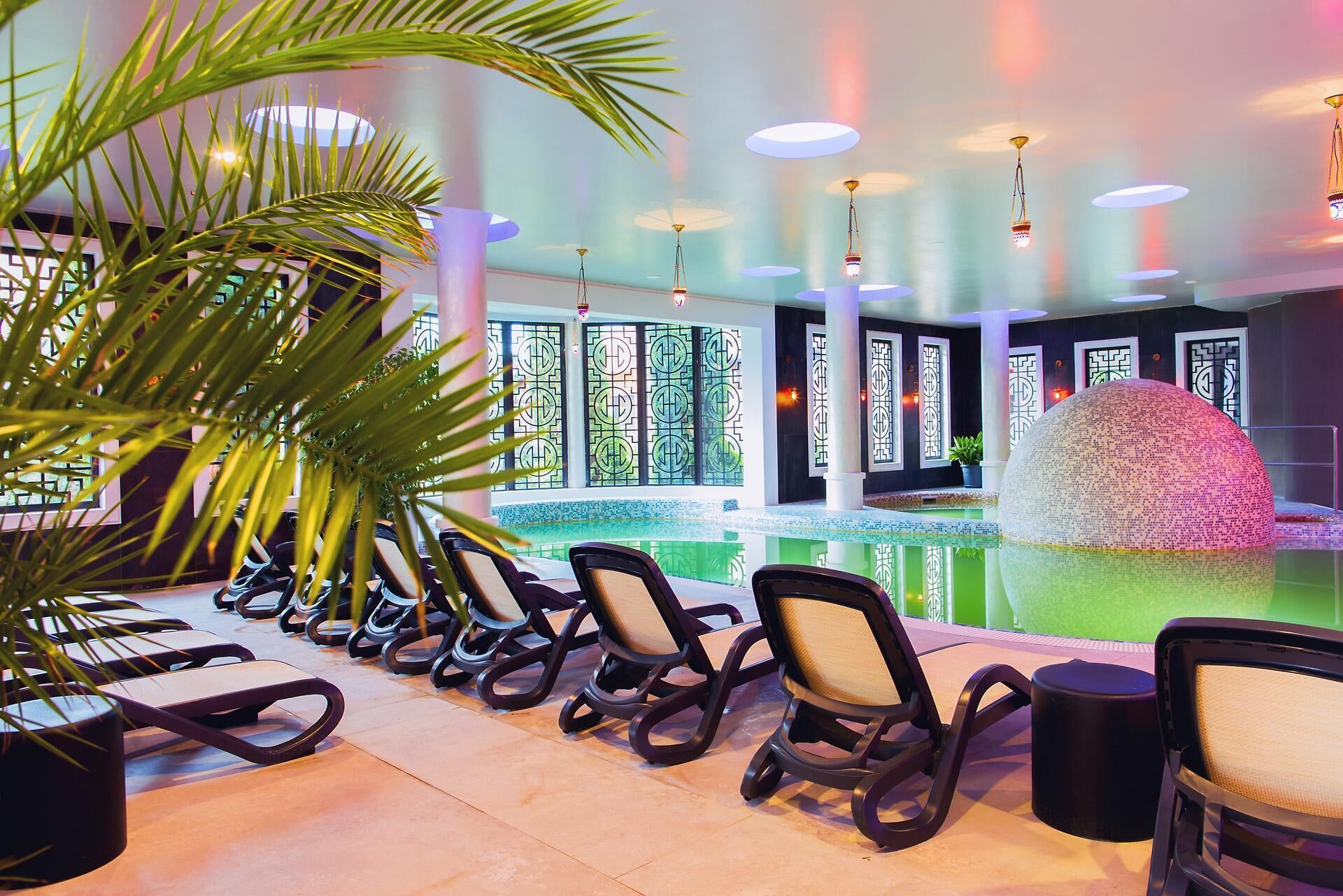 A poolside area with lounge chairs, a decorative sphere, and a tiled floor.